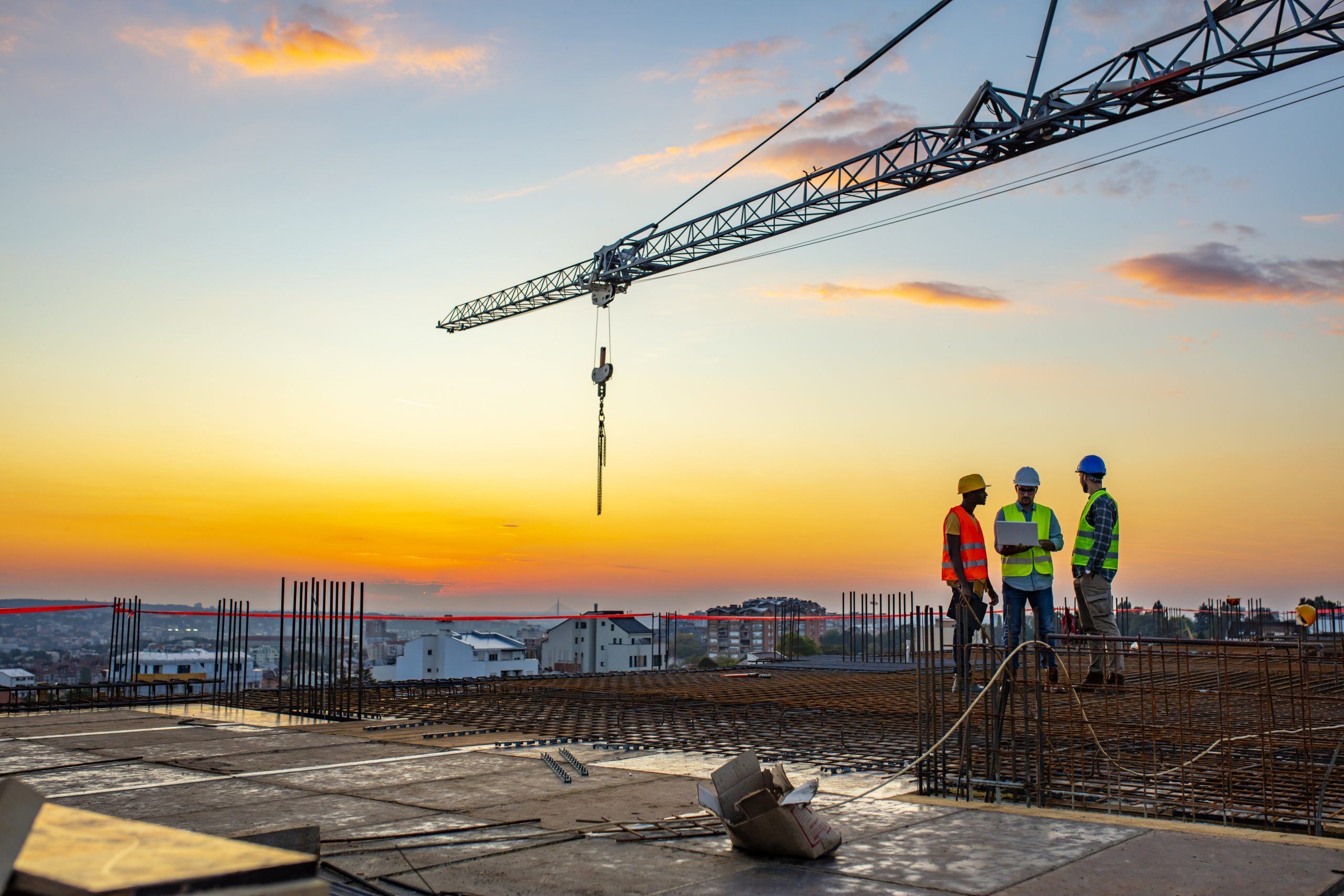 Three construction workers under a tower crane at sunset on a building site