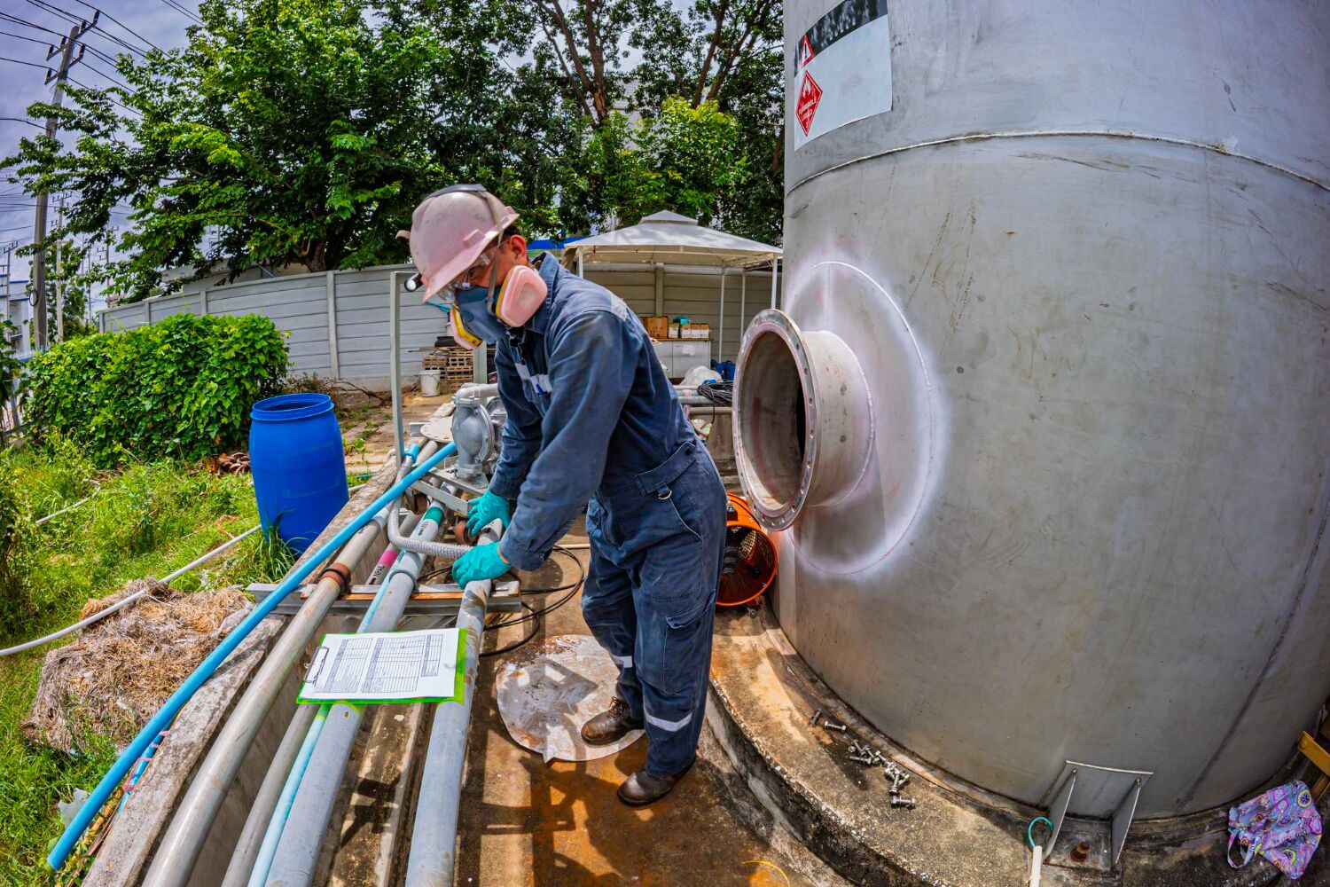 Technician in hard hat checking pipework at a storage tank